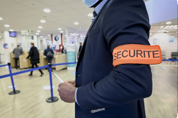 Security agent standing at the entrance of a corporate building, watching over the area. The agent's face is not visible.
